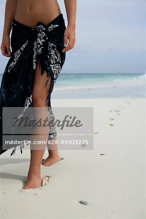 Jeune fille marchant le long de la plage, empreintes sur le sable