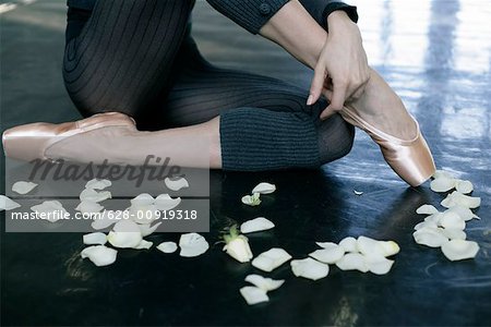 A female ballet dancer sitting next to rose petals on the floor