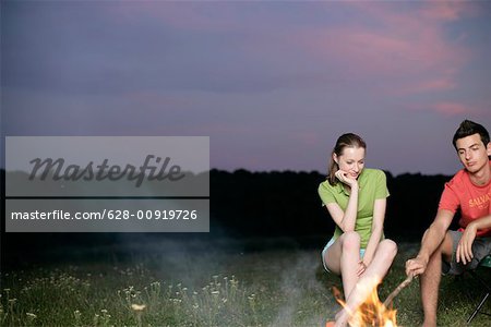 Jeune couple assis devant un feu de camp