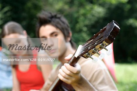 Young couple sitting side by side while he is playing the guitar