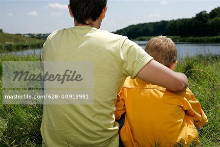 Père et fils, assis à côté d'un lac