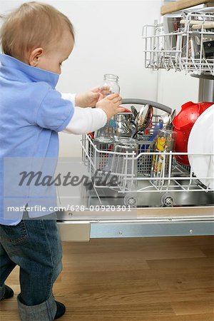 Baby boy taking a glass bottle from a dishwasher