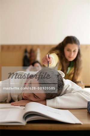 Teenage boy sleeping in a classroom, teenage girl tapping him