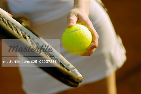 Mid section view of a woman holding a tennis racket and a tennis ball
