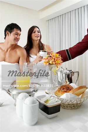 Person's hand serving tea to a young woman and a mid adult man on the bed