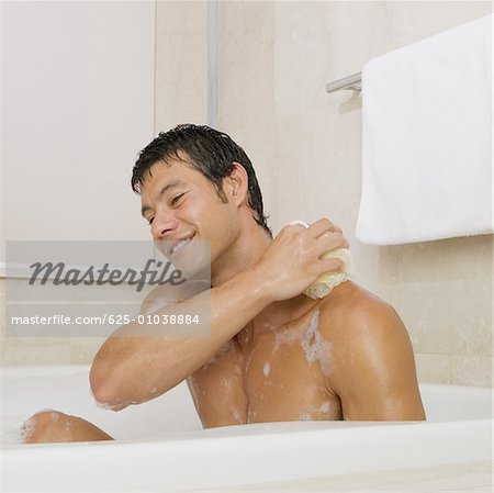 Mid adult man scrubbing his body in the bathtub