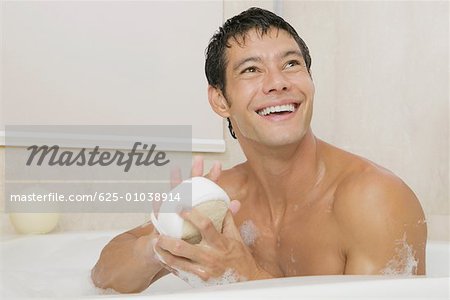 Close-up of a young man holding a loofah in a bathtub