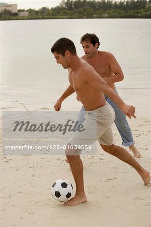 Two mid adult men playing soccer on the beach