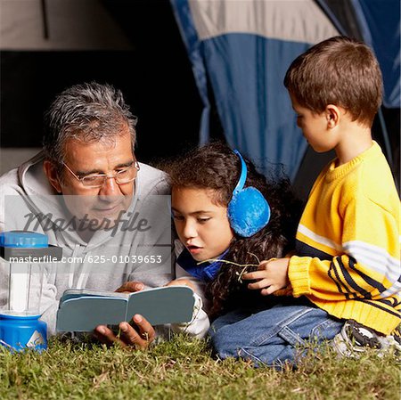 Side profile of a boy looking at his grandfather and sister reading a book