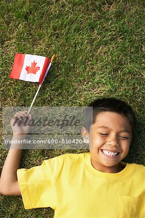 Portrait de garçon couché sur l'herbe, tenant le drapeau canadien