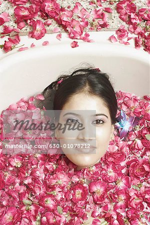 High angle view of a young woman lying in a bathtub covered with flower petals