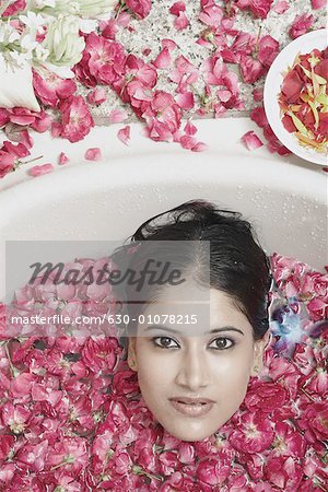 High angle view of a young woman lying in a bathtub covered with flower petals