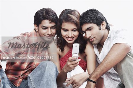 Nahaufnahme von einer jungen Frau und zwei junge Männer, die ein Mobiltelefon betrachten
