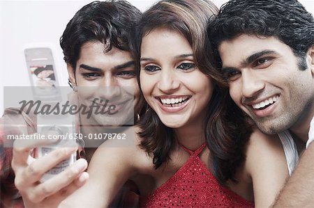 Close-up of a young woman with two young men taking a photograph of themselves