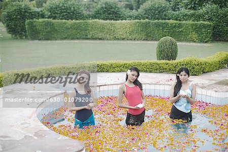 Portrait de trois jeunes femmes tenant des bougies, debout dans une piscine