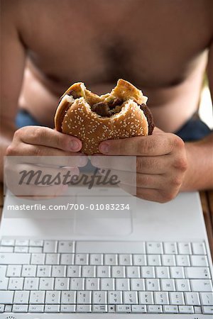 Man Eating Hamburger and Using Laptop