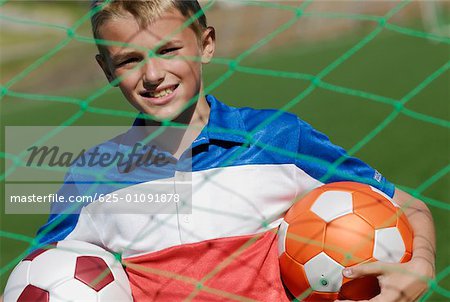 Portrait of a soccer player standing behind the net and holding two soccer balls