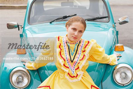 Portrait of a young woman sitting on the bumper of a car