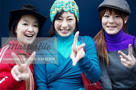 Portrait de trois jeunes femmes faisant le signe de la paix