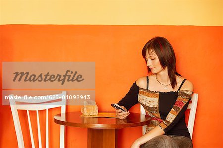 Junge Frau sitzt an einem Tisch mit einem Mobiltelefon