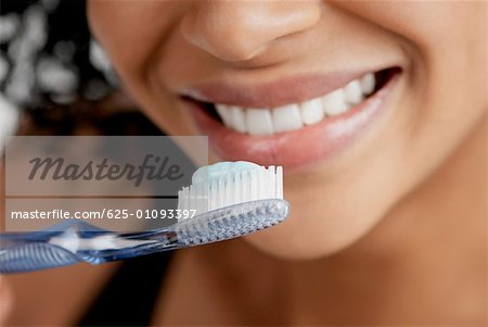 Gros plan d'une brosse à dents avec dentifrice en face de la bouche d'une jeune femme