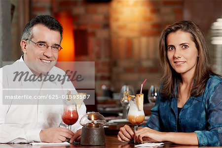 Portrait d'un couple adult moyen assis dans un restaurant avec deux verres de pina colada