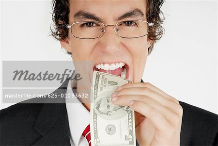 Portrait d'un homme d'affaires mettant un billet d'un dollar dans sa bouche