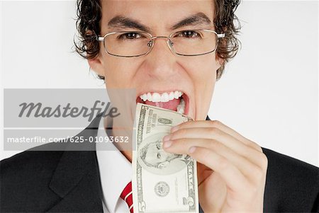 Portrait of a businessman putting a dollar bill into his mouth