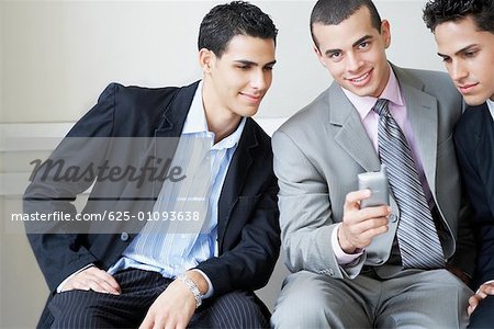 Portrait of a businessman holding a mobile phone with two businessmen looking at it