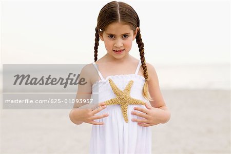 Portrait of a girl standing on the beach and holding a starfish