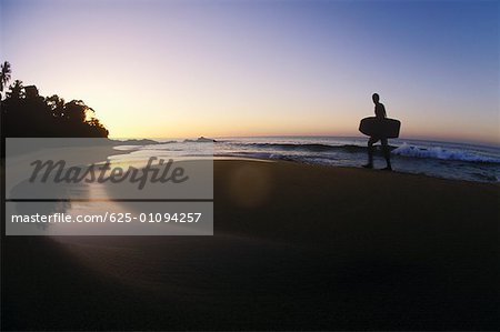 Silhouette of a person carrying a surfboard on the beach, Caribbean