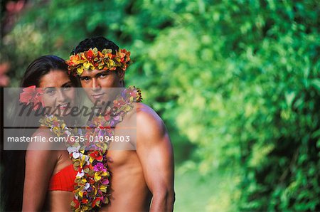 Portrait of a young couple standing together wearing garlands, Hawaii, USA