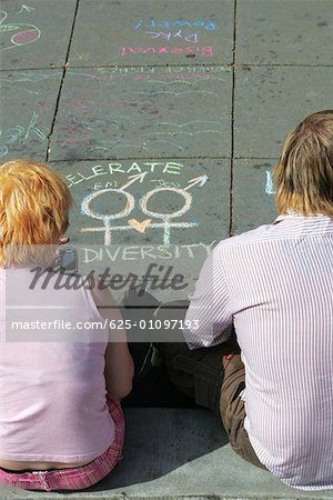 High angle view of a man and a woman sitting on the street near a chalk drawing