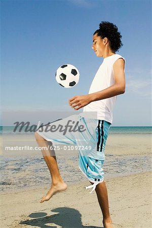 Side profile of a teenage boy playing with a soccer ball on the beach