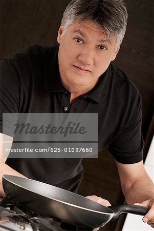 Portrait of a senior man holding a frying pan in the kitchen