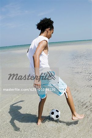 Rear view of a teenage girl playing with a soccer ball on the beach