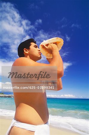 Profil de côté d'un jeune homme soufflant une conque sur la beach, Hawaii, USA