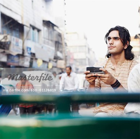 Young man sitting in a rickshaw and holding a mobile phone