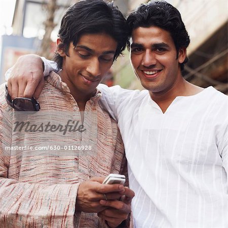 Portrait d'un jeune homme souriant avec un autre en utilisant un téléphone mobile