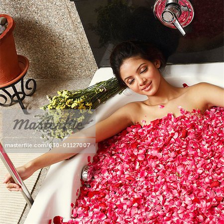Vue grand angle d'une jeune femme dans une baignoire pleine de pétales de roses