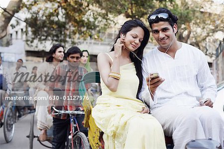 Young couple sitting in a rickshaw and listening to an MP3 player