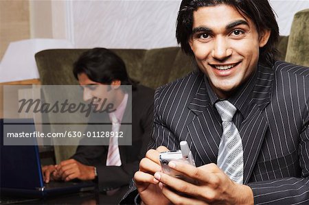 Portrait d'un homme d'affaires en tenant un téléphone mobile avec un autre homme d'affaires à l'aide d'un ordinateur portable derrière lui