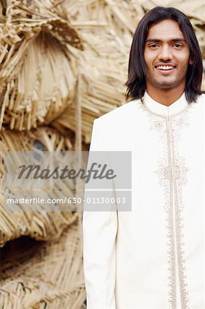 Portrait of a young man standing in front of a hut and smiling