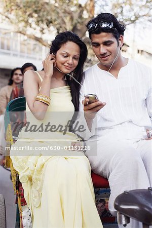 Young couple sitting in a rickshaw and listening to an MP3 player