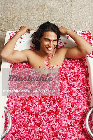 Portrait of a young man lying in a bathtub filled with rose petals and smiling