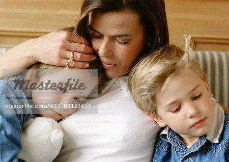 Frau zwischen zwei Kinder, hält kleinen Mädchens Kopf an ihre Brust, kleiner Junge gelehnt, Nahaufnahme