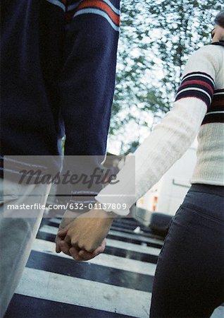 Young couple holding hands at pedestrian crossing, close up, rear view