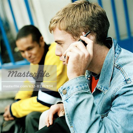 Young men sitting together, close up of one on cell phone, side view
