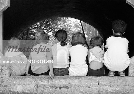 Children sitting under arch, viewed from the back, b&w