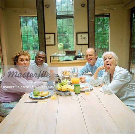 Four mature people sitting at table, sticking out tongues